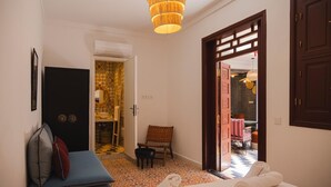 Una camera d'albergo con un letto, una sedia, un tavolino, una porta in legno e vista su una sala da pranzo attraverso una porta aperta.