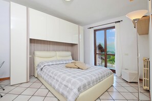 A bedroom with a bed, a window with a view, a radiator, and a lamp. - Dalia (Colico)