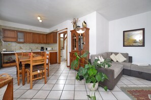 A kitchen with wooden cabinets, a dining table with chairs, a living area with a sofa, and a potted plant. - Dalia (Colico)