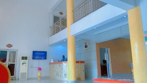 A hotel lobby with a reception desk, a TV screen, a large pillar, and a balcony. - ROSES REGENCY HOTEL & SUITES (Abuja)