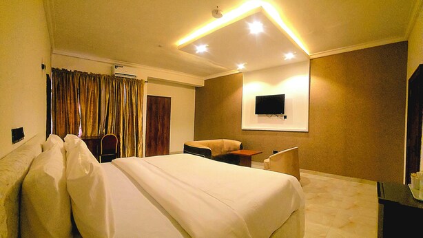 A hotel room with a large bed, a flat-screen TV mounted on the wall, and a desk with a chair. - ROSES REGENCY HOTEL & SUITES (Abuja)