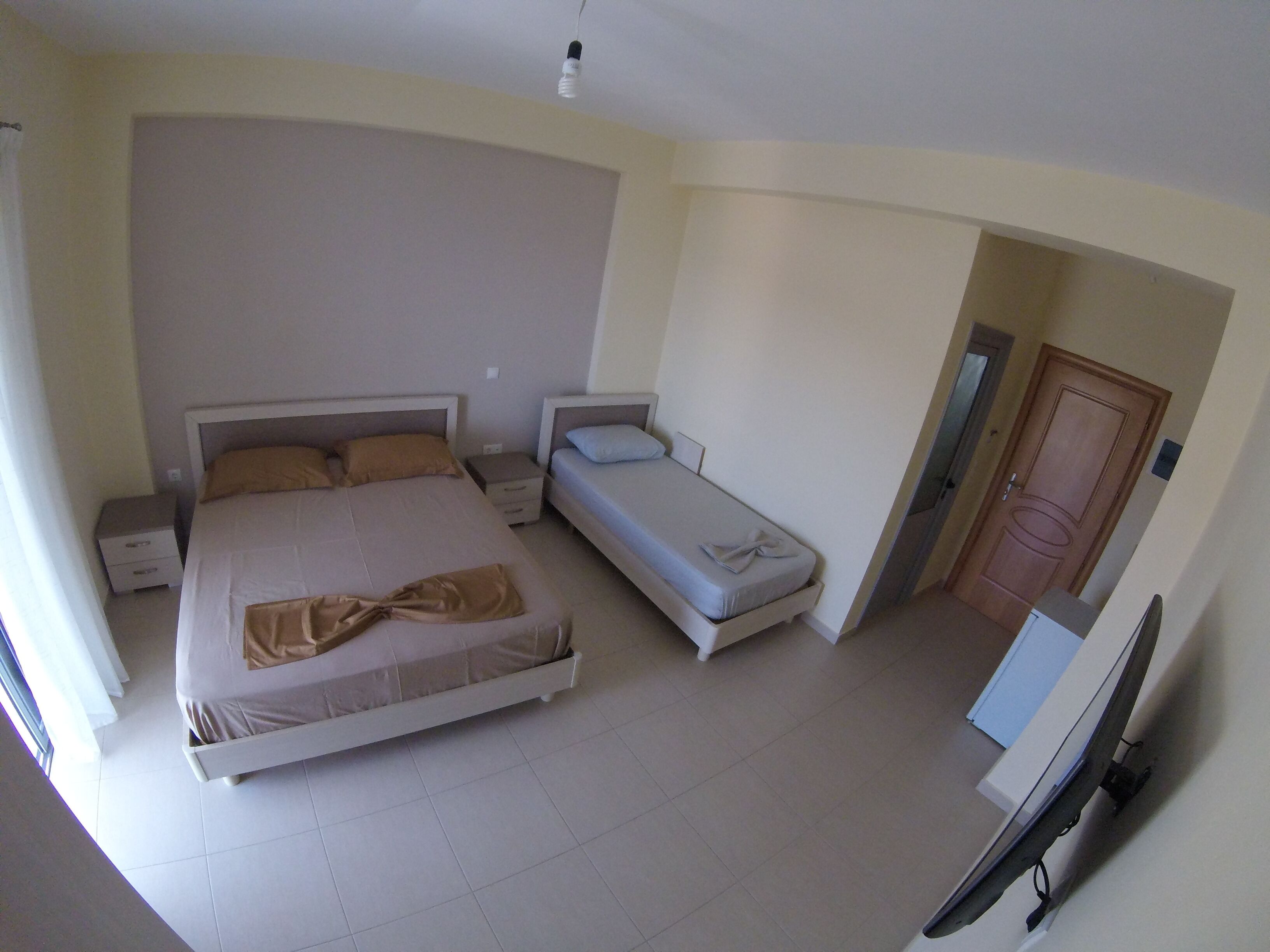 A bedroom with a large bed, a smaller bed, a nightstand, a TV, and a door.
