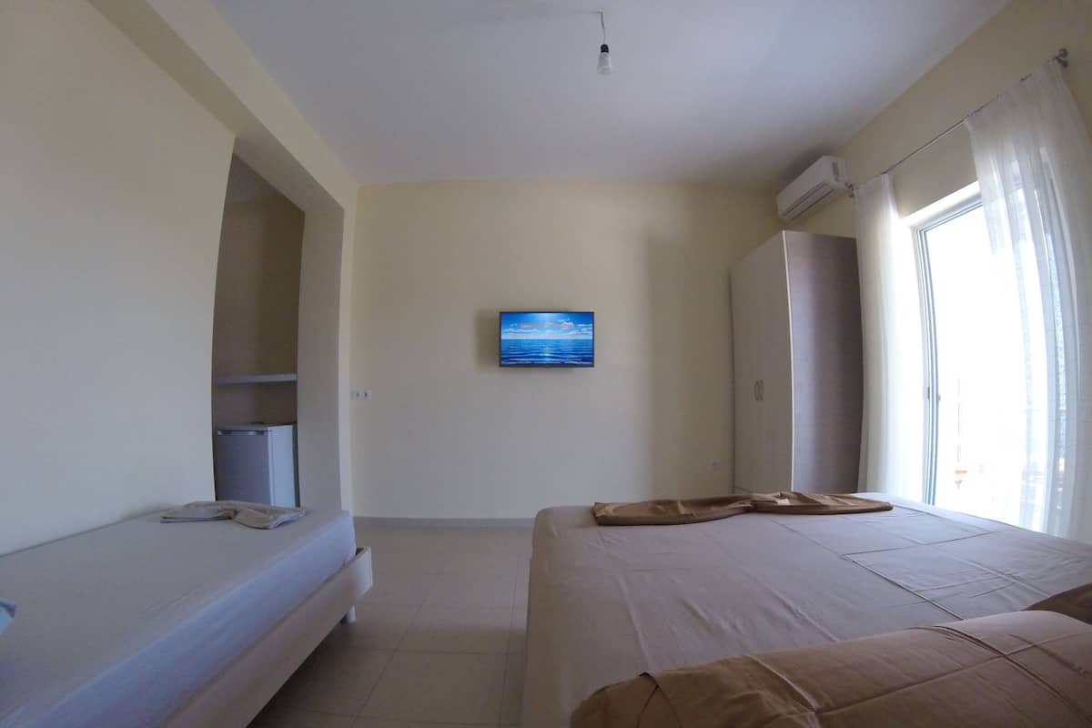 Un dormitorio con cama, una mesita, un televisor y una ventana con cortinas.