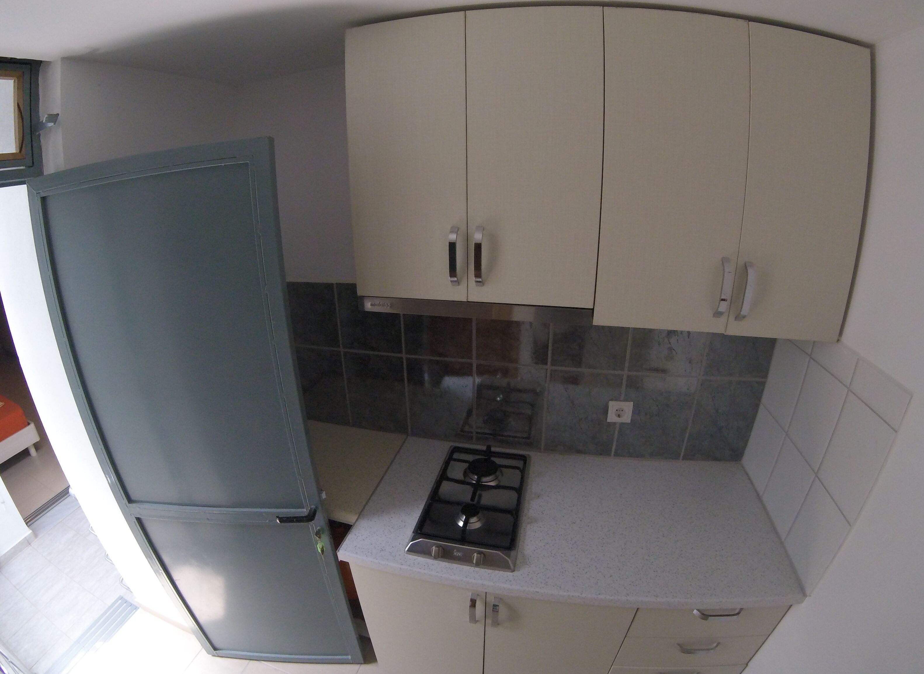 Una cocina compacta con refrigerador, estufa a gas y armarios de color claro.