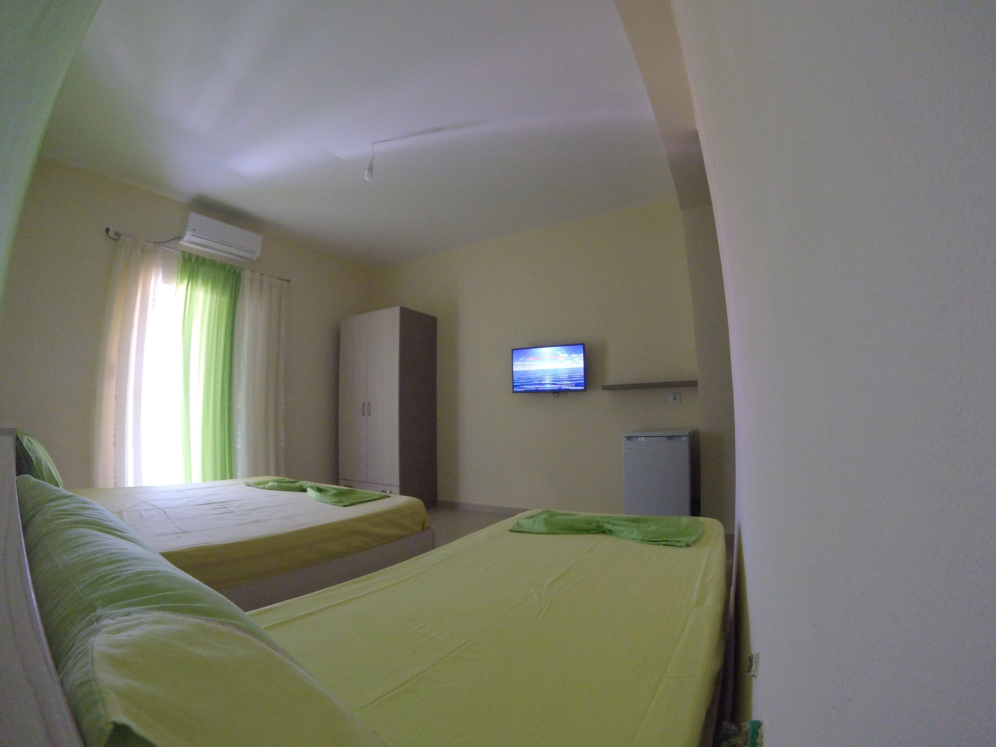 Une chambre d’hôtel avec deux lits simples, une armoire, une télévision et un réfrigérateur.