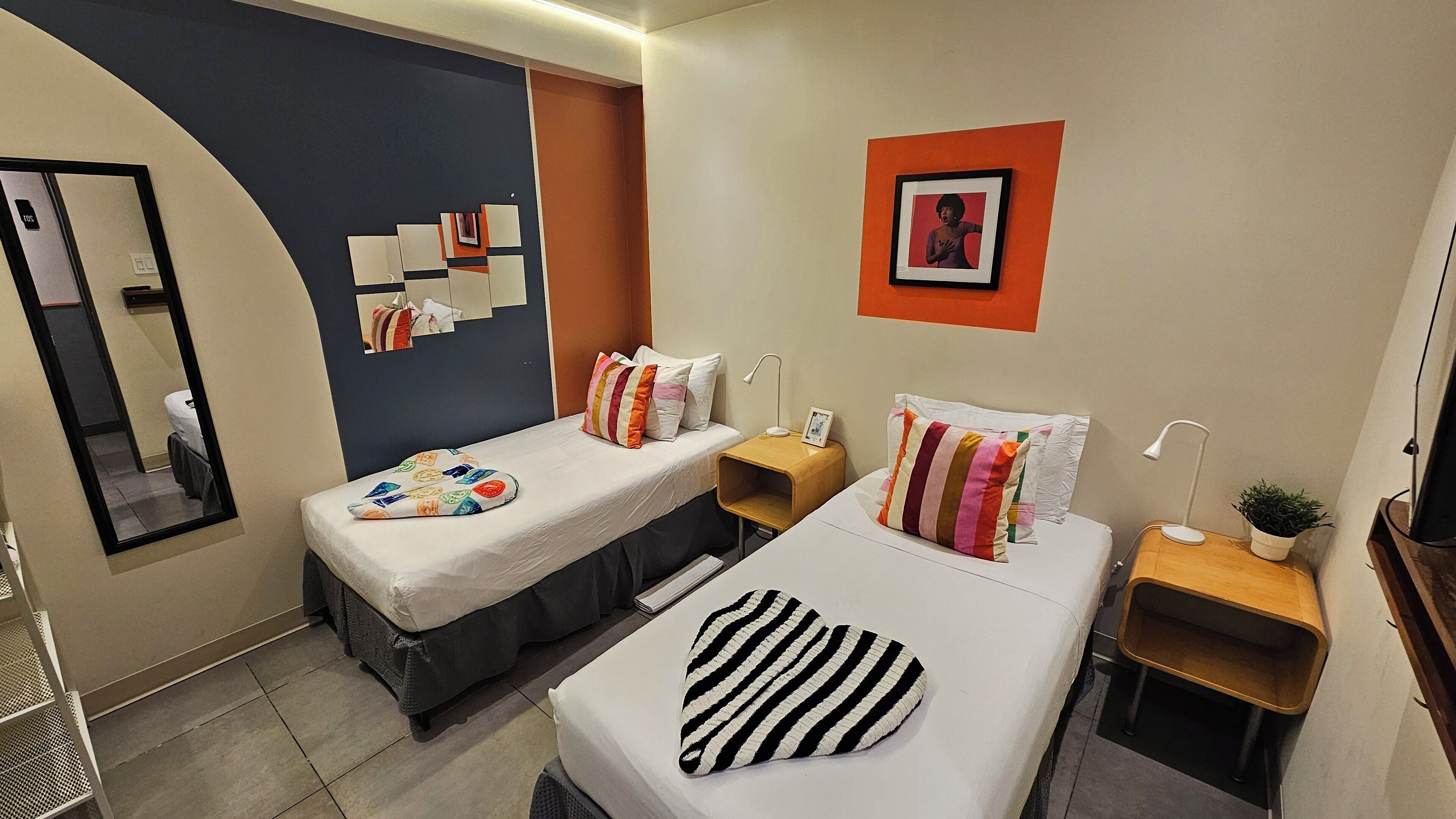 A hotel room with two beds, a mirror, a wall-mounted picture, and a small plant.
