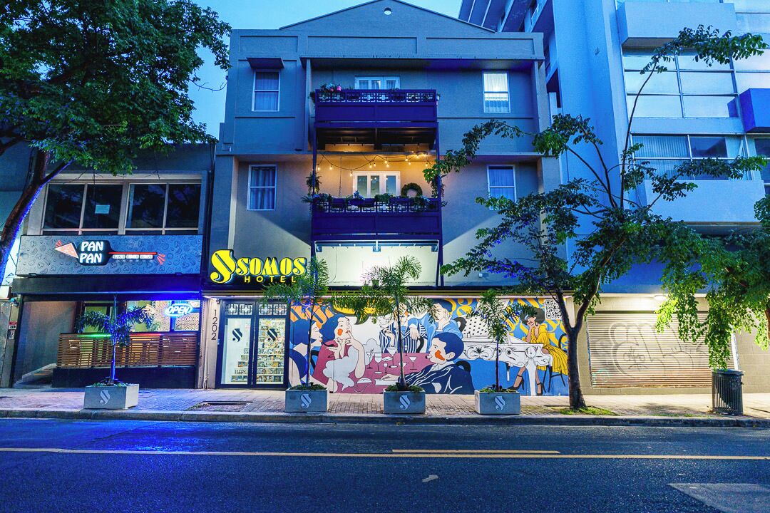 Un hotel con un murale sulla facciata, un ingresso ben visibile e un balcone decorato con luci a stringa.