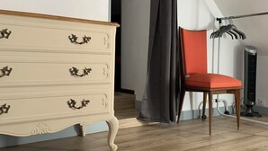 Una habitación con un aparador de madera, una silla roja, un radiador negro y una cortina gris.