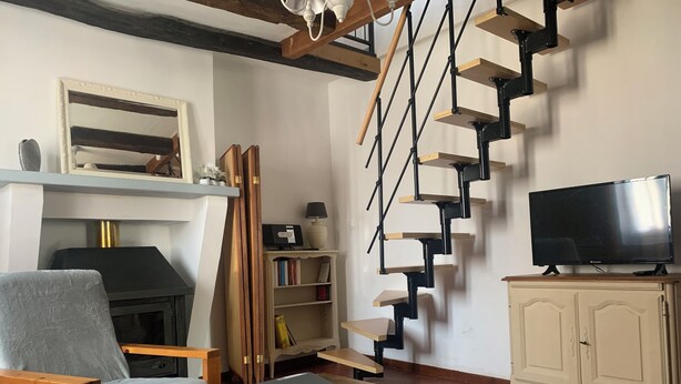 Una sala de estar con chimenea, televisor, estantería y escalera.