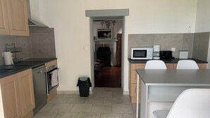 Una cocina moderna con microondas, cafetera y un pequeño comedor con sillas blancas.