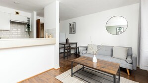 A modern living room with a grey sofa, a wooden coffee table, and a dining area with a table and chairs. - The Bridge Flats (London)