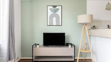 Ein modernes Wohnzimmer mit Flachbildfernseher auf einer schlichten Kommode, einer Stehlampe und einem gerahmten abstrakten Kunstwerk an der Wand.