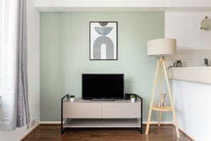 Una sala de estar moderna con un televisor de pantalla plana sobre un mueble minimalista, una lámpara de pie y una obra de arte abstracto enmarcada en la pared.