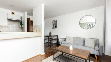 A modern living room with a grey sofa, a wooden coffee table, and a dining area with a table and chairs.