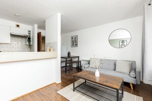 A modern living room with a grey sofa, a wooden coffee table, and a dining area with a table and chairs. - The Bridge Flats (London)