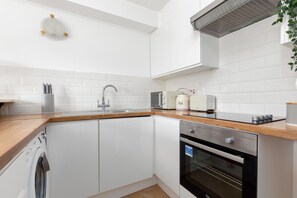 Una cocina compacta con armarios blancos, horno de acero inoxidable, microondas y tostadora.