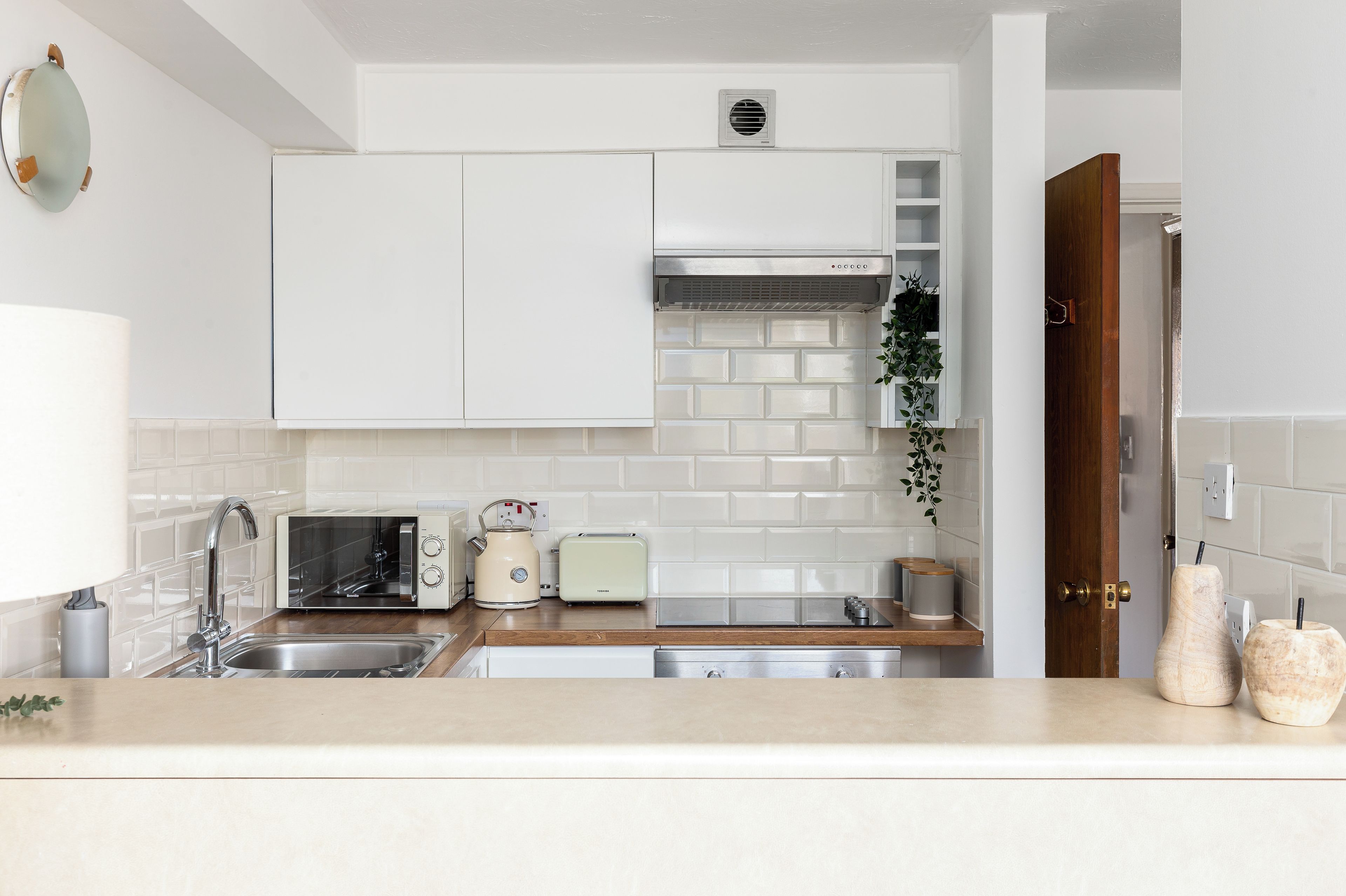 A modern kitchen with white cabinets, a stainless steel sink, a microwave, a toaster, and a coffee maker.