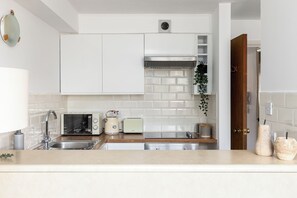 A modern kitchen with white cabinets, a stainless steel sink, a microwave, a toaster, and a coffee maker. - The Bridge Flats (London)