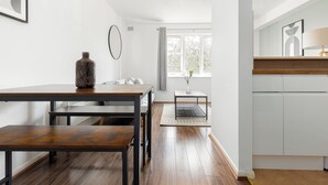 A modern kitchen with white cabinets, a wooden countertop, and a dining area with a wooden table and bench. - The Bridge Flats (London)