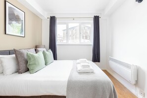A neatly made bed with pillows, a window with curtains, and a radiator.