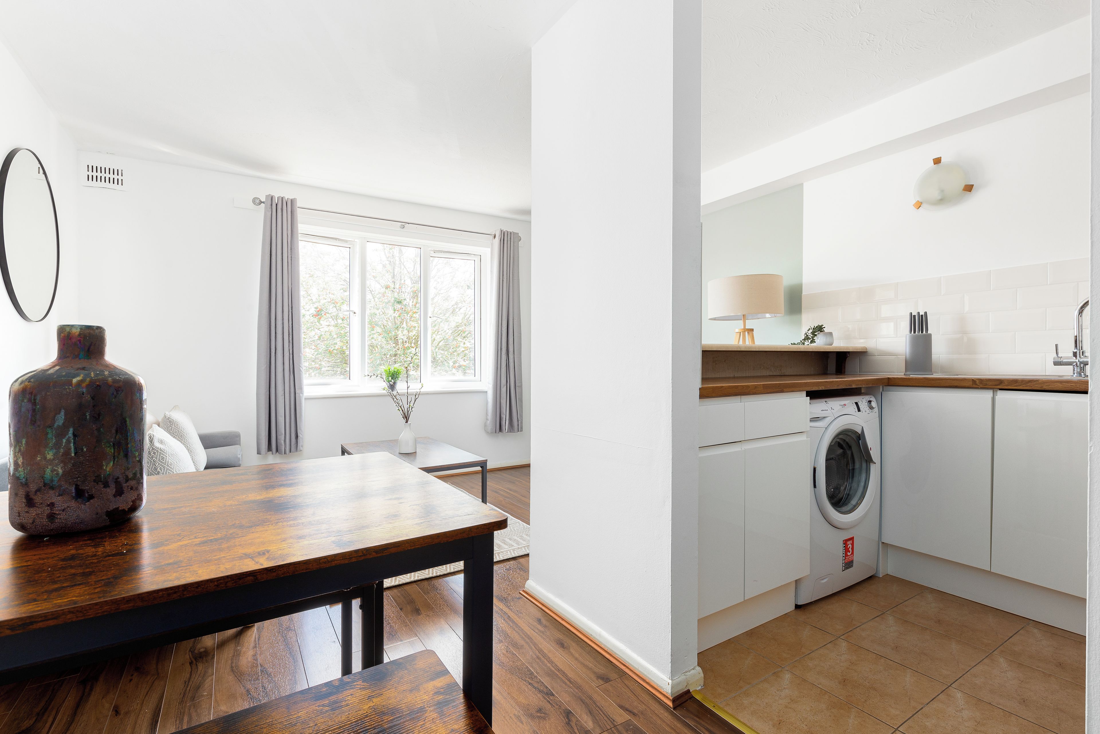Eine moderne Küche mit Waschmaschine, einem Holzes Esstisch und einem Fenster mit Vorhängen.