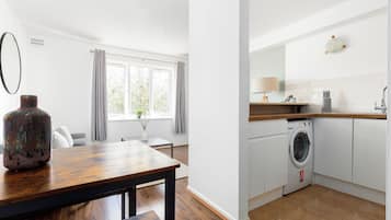 Eine moderne Küche mit Waschmaschine, einem Holzes Esstisch und einem Fenster mit Vorhängen.