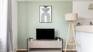 A modern living room with a flat-screen TV on a minimalist console, a floor lamp, and a framed abstract artwork on the wall. - The Bridge Flats (London)