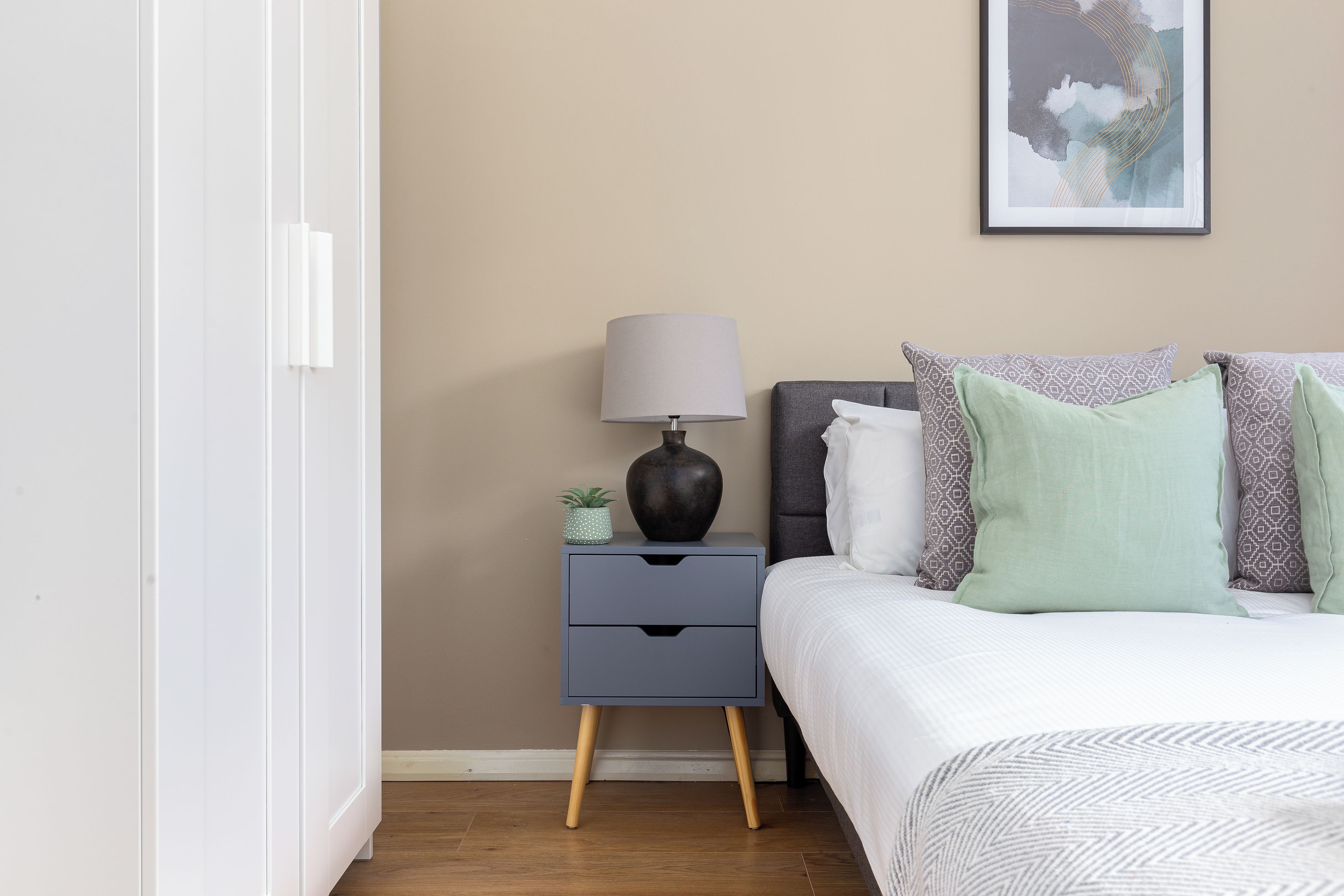 A bedroom with a bed, a nightstand with a lamp, and a wall-mounted painting.