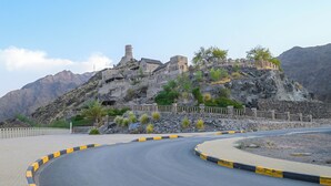A winding road leading to a historic stone fortress with a prominent tower, surrounded by rocky terrain and sparse vegetation. - Najd Al Meqsar By Sharjah Collection (Khor Fakkan)
