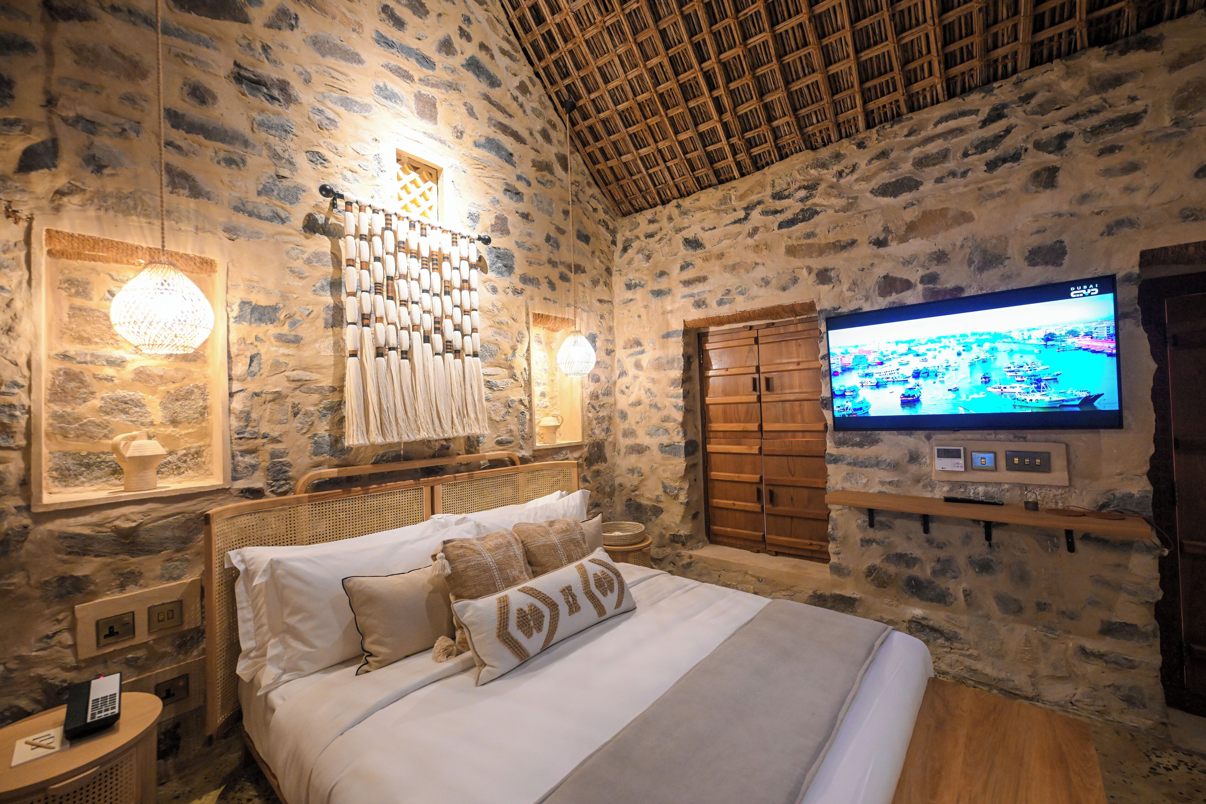 Habitació amb parets de pedra, un llit, una televisió penjada a la paret i un sostre de fusta.