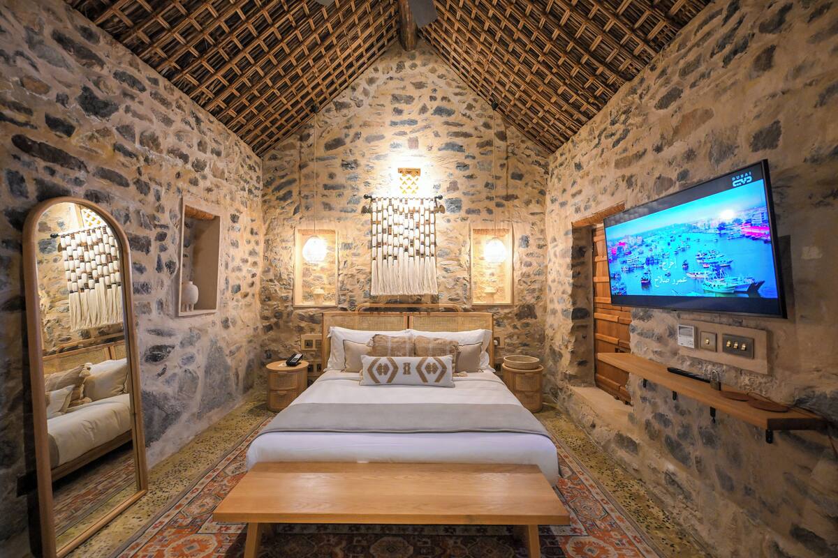 A stone-walled room with a bed, a TV, and a wooden bench.