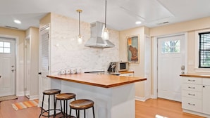 A kitchen with a central island, bar stools, a microwave, and a hanging light fixture. - Locust Garden, A North Downtown C'ville Guesthouse (Charlottesville)