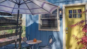 A blue house with a yellow door, a small patio with a table and chairs, and a purple umbrella. - Locust Garden, A North Downtown C'ville Guesthouse (Charlottesville)