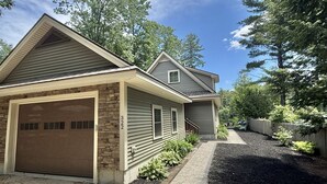 A two-story house with a garage, a stone accent wall, and a driveway leading to the entrance. - WATERFRONT NEWER HOME WITH A DOCK.  4 BEDROOM 2 BATH.   (Sebago)