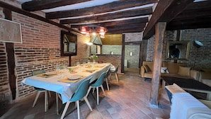 Ein Essbereich mit einem langen Tisch, gedeckt für sechs Personen, Ziegelwänden, freiliegenden Holzbalken und einer Steinwand im Hintergrund.