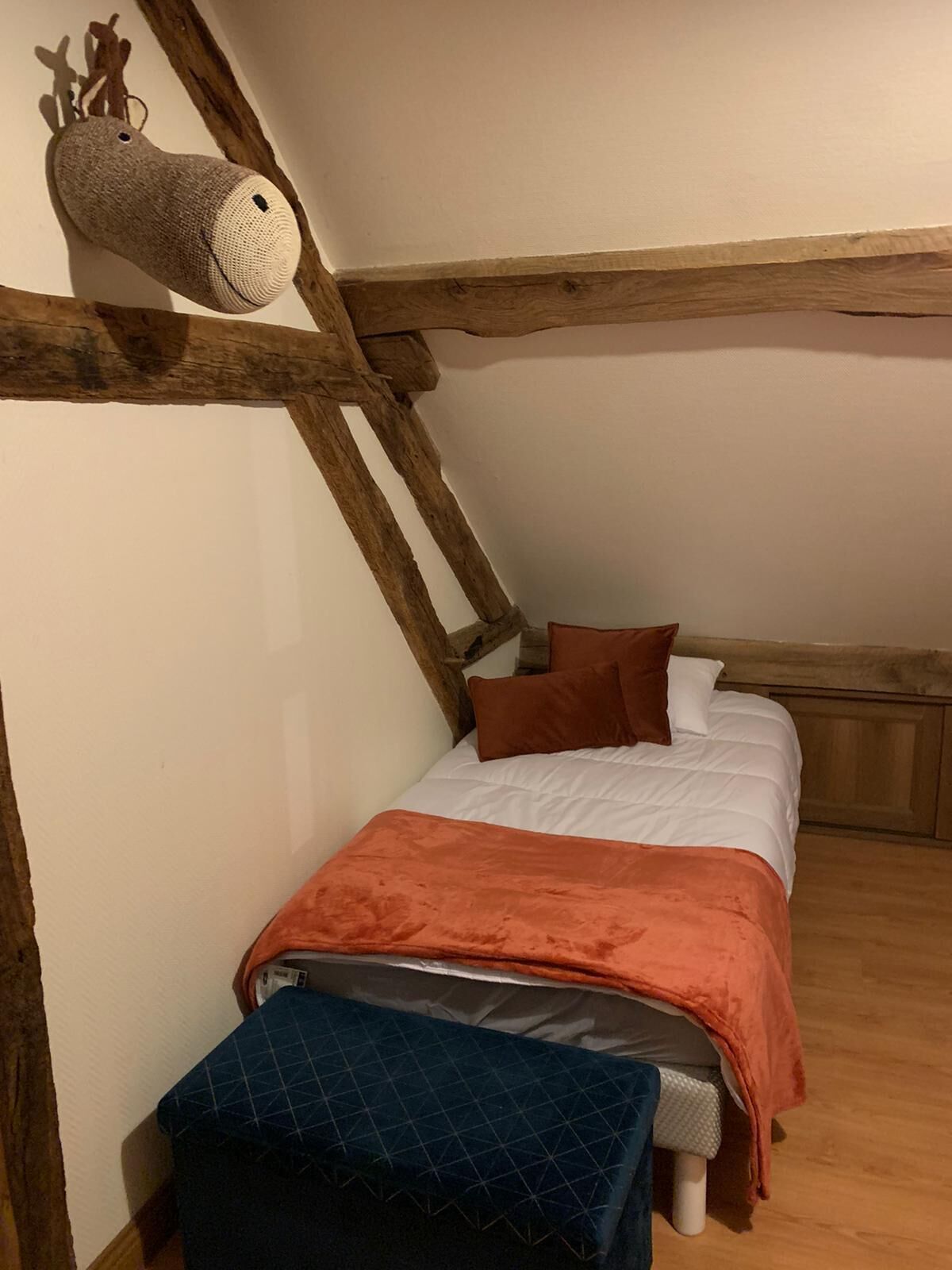 Un dormitorio pequeño y acogedor con techo inclinado, cabecero de madera, cama con ropa de cama blanca y marrón, y una alfombra pequeña.