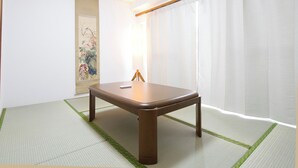 Una stanza con pavimento in tatami, un tavolo in legno, una lampada da terra e un quadro appeso al muro.