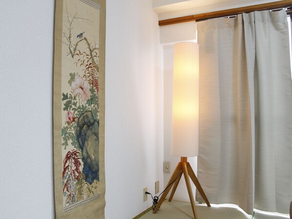 A room with a traditional Japanese-style painting on the wall, a standing lamp, and a window with curtains.