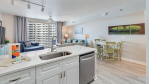 Una cocina moderna con lavavajillas integrado, un comedor con mesa y sillas, y una sala de estar con sofá y vistas a un edificio alto.