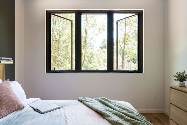A bedroom with a bed, a bedside table, a window with a view of trees, and a dresser. - 9 Forested Acres  Hot Tub  4 miles to downtown Asheville (Asheville)