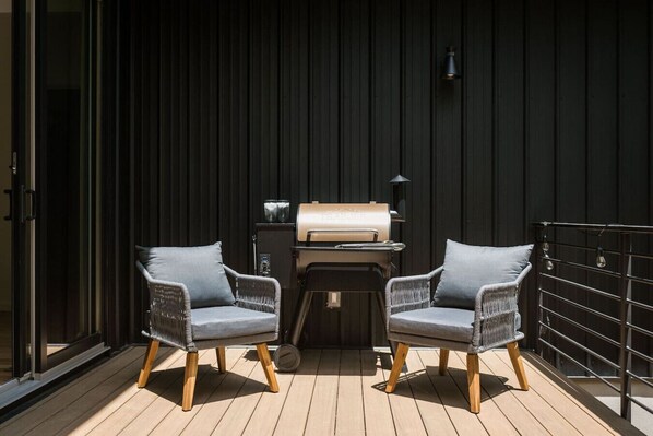 Una terrazza con due poltrone in vimini, un barbecue e un muro in legno scuro.