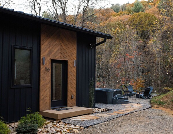 A modern cabin with a wooden exterior, a black door, and a gravel pathway leading to outdoor seating.