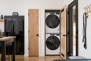 A compact kitchen with a refrigerator, coffee machine, and a wooden door leading to a laundry area with two washing machines. - 9 Forested Acres  Hot Tub  4 miles to downtown Asheville (Asheville)