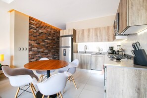 A modern kitchen with a central island, a dining area with a round table and chairs, and a brick accent wall. - 1BR w/ Rooftop Pool, Bar + City Views | Old Town (Puerto Vallarta)