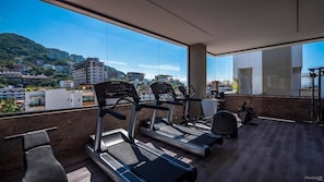 A gym with treadmills and exercise equipment, large windows with a city view, and a brick wall.