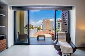 A modern living room with a sliding glass door leading to a balcony, a sofa, a wicker chair, and a small table.