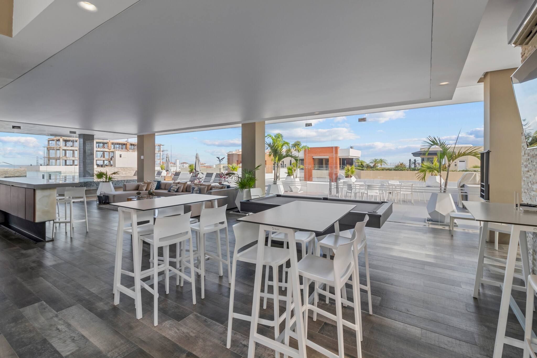 A spacious outdoor dining area with multiple tables and chairs, large windows offering a view of the cityscape, and a modern architectural design.