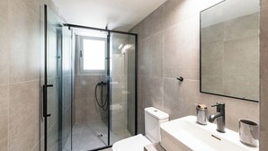 Une salle de bain moderne avec une douche à parois de verre, des toilettes blanches et un lavabo surmonté d’un grand miroir.