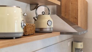 Une cuisine équipée d’une bouilloire, d’un grille-pain et d’une machine à café, le tout posé sur une étagère en bois.