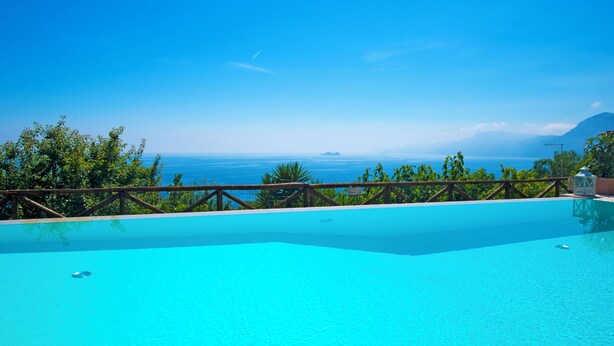 Ein klares, blaues Schwimmbecken mit einer Holzterrasse und Blick auf den Ozean.
